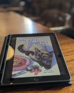 Cozy Mystery One Taste Too Many on an ipad at a coffee shop